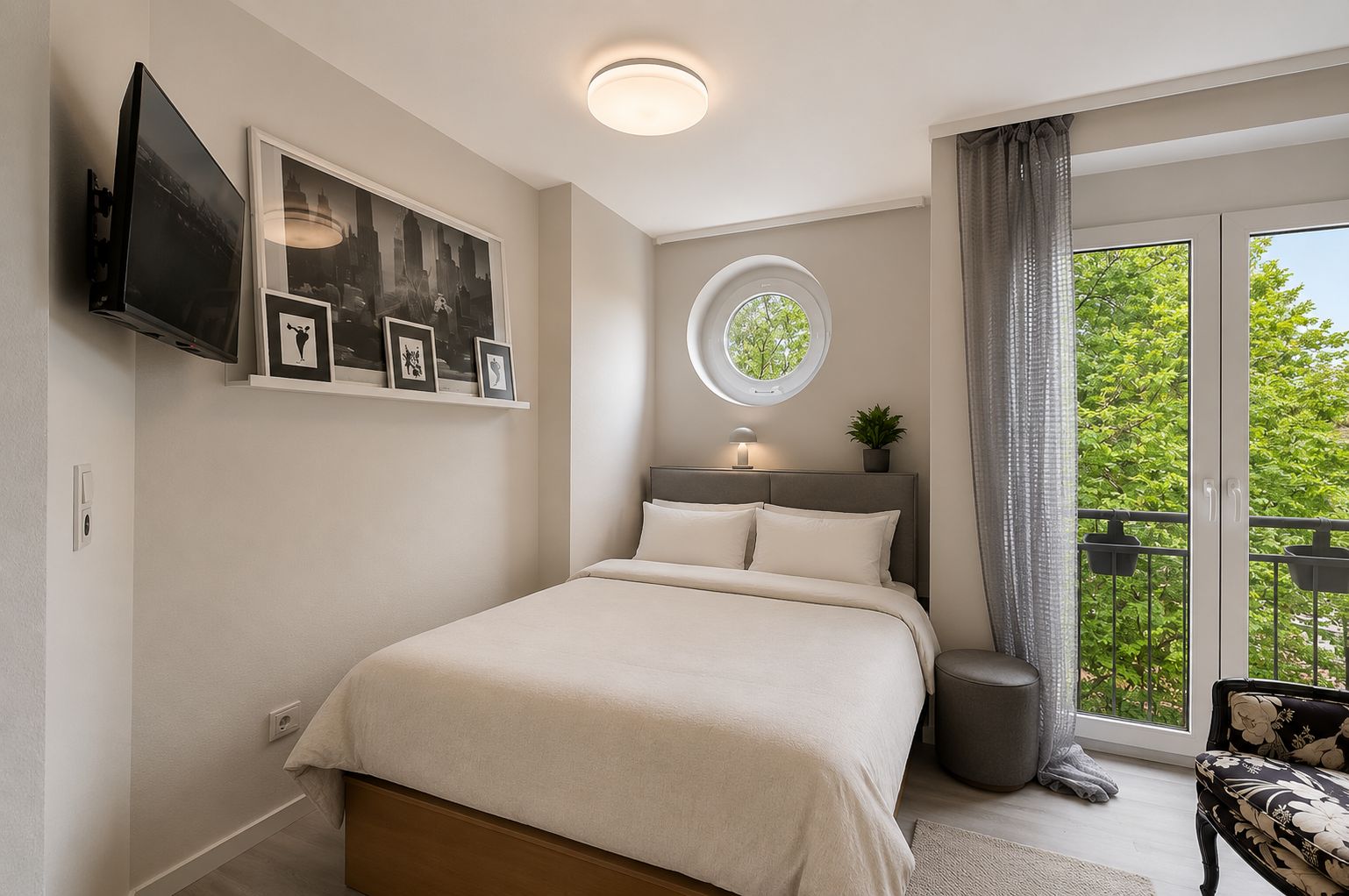 Modernes Schlafzimmer mit Doppelbett, Wandkunst, Fernseher und bodentiefer Fensterfront mit Blick auf Bäume.