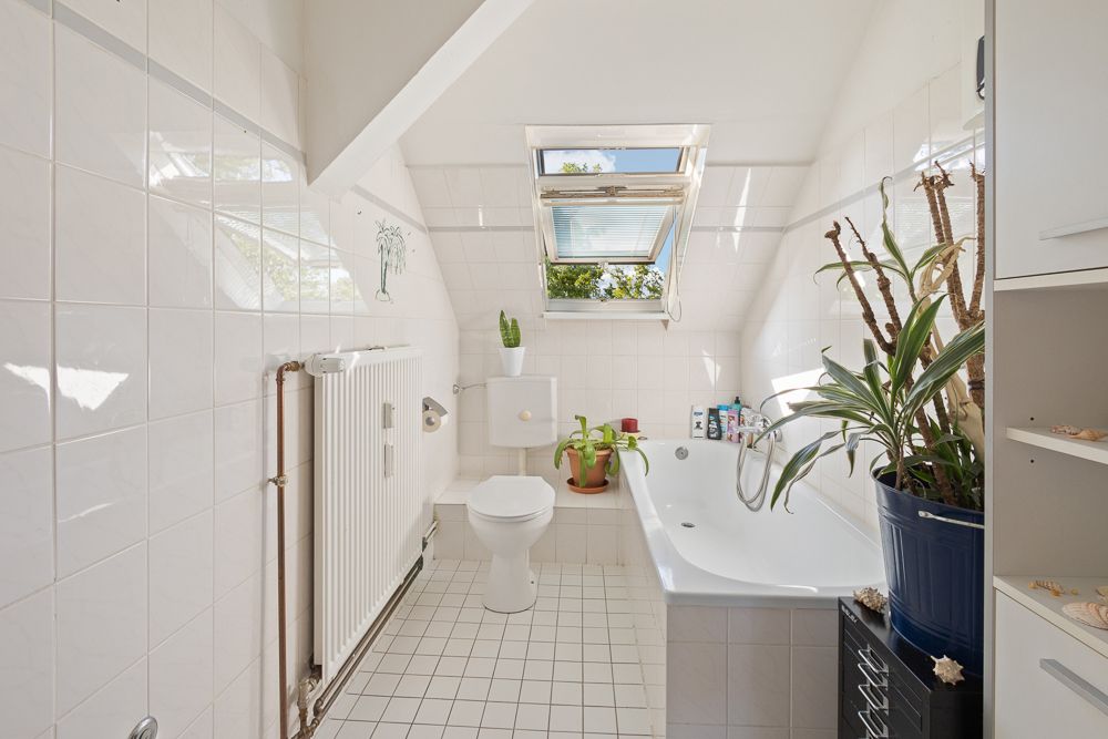 Helles Badezimmer mit Badewanne, WC, Pflanzen und Dachfenster.