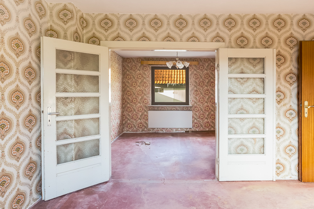 Leerer Raum mit gemusterten Tapeten, Glastüren und Fenster, rosa Boden.