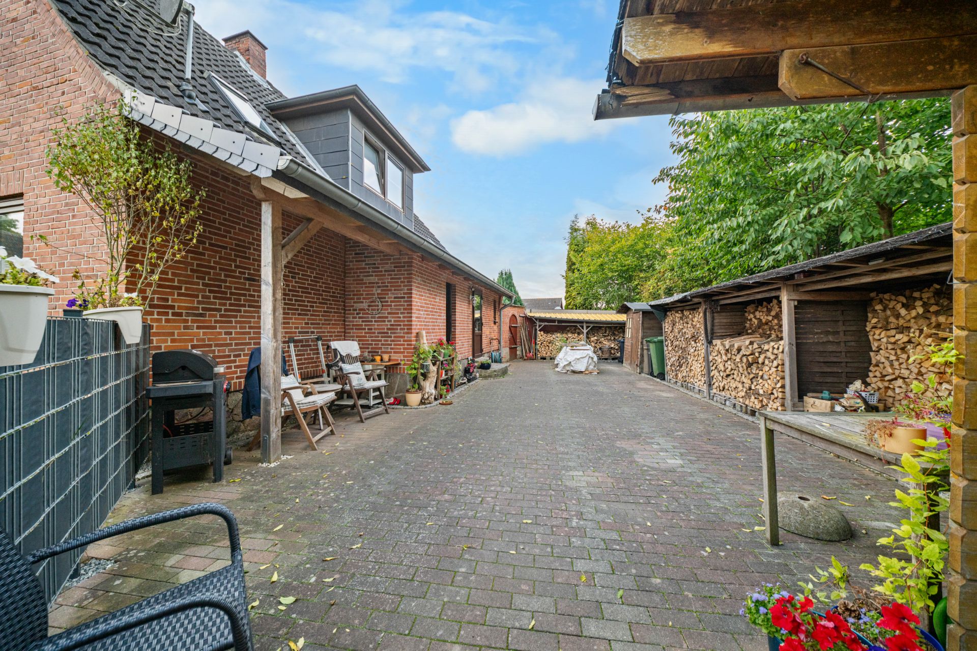 Gepflasterter Innenhof mit Sitzgelegenheiten, Pflanzen und gestapeltem Brennholz neben einem Backsteinhaus.