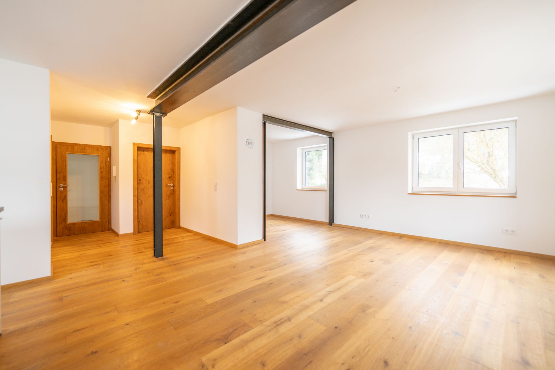 Heller Raum mit Holzboden, weißen Wänden, zwei Fenstern und Holztüren.