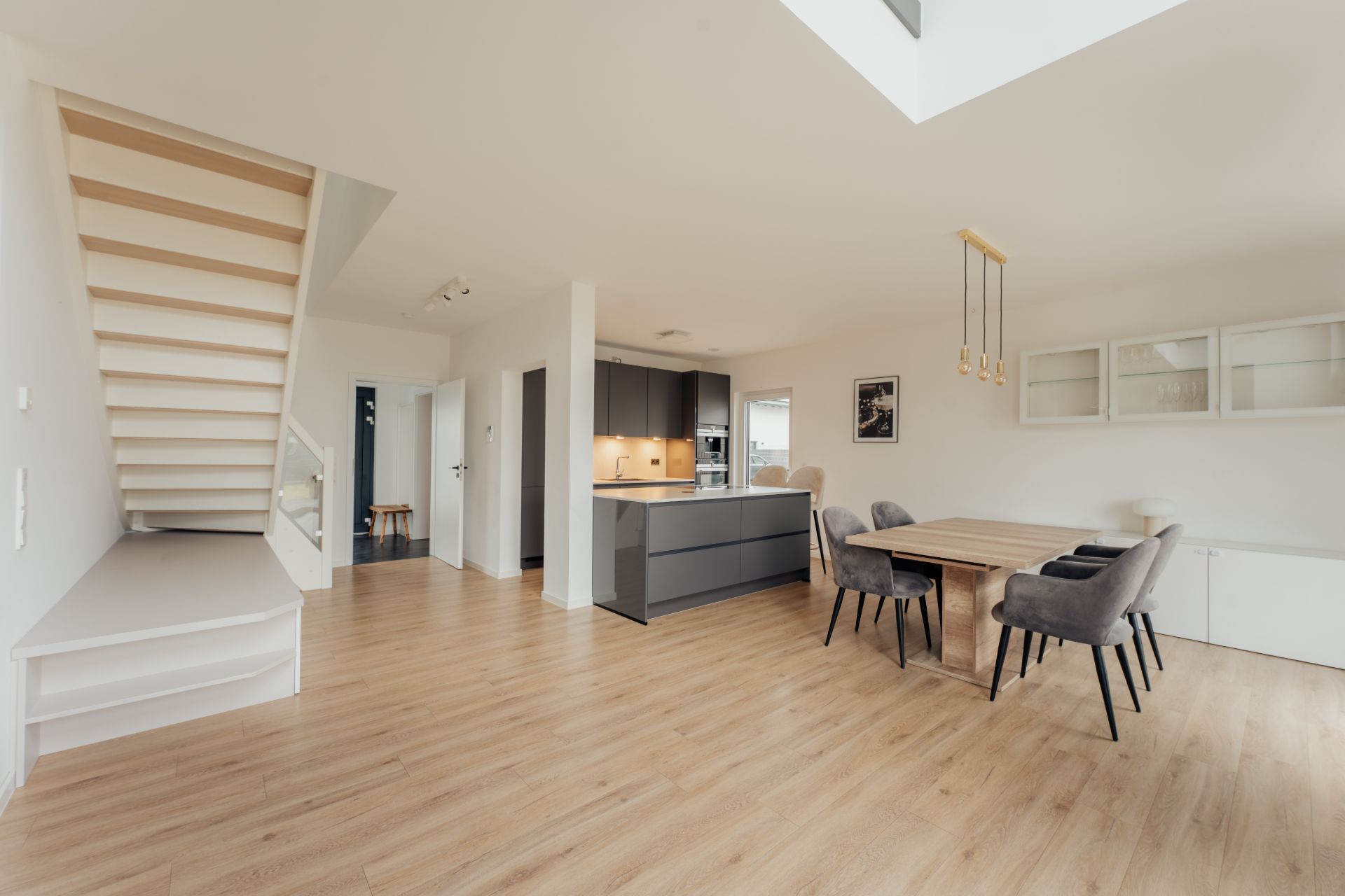 Helles Wohnzimmer mit Holzboden, Esstisch, moderner Küche und offener Treppe.