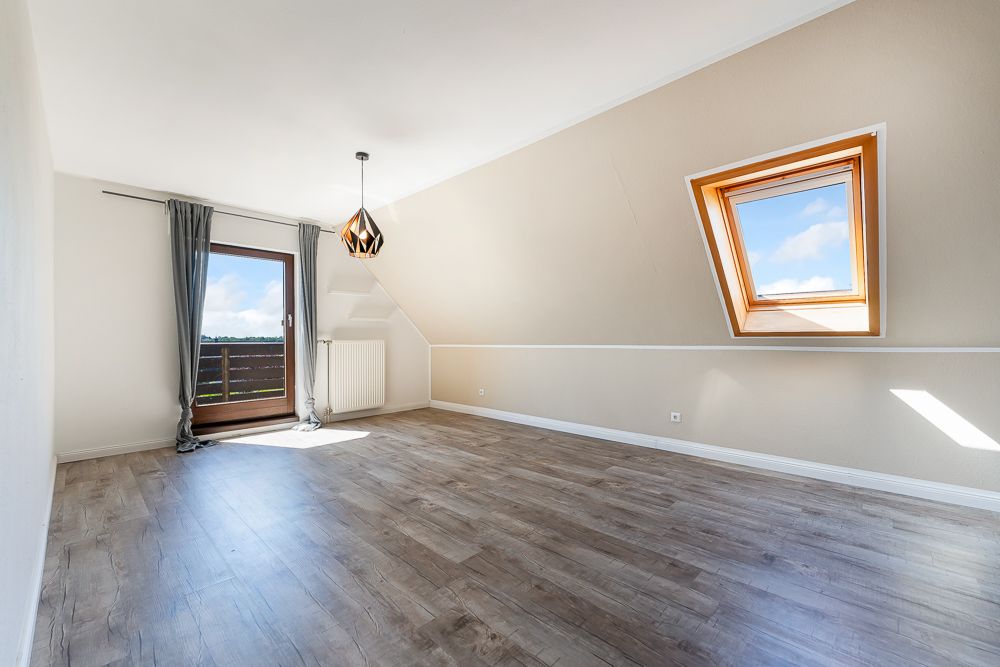 Helles Zimmer mit Holzfußboden, Dachfenster und Glastür zu einem Balkon.