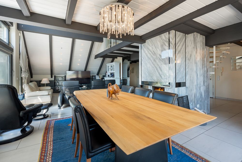 Wohnzimmer mit Holztisch, schwarzen Stühlen, Kamin und modernem Kronleuchter.