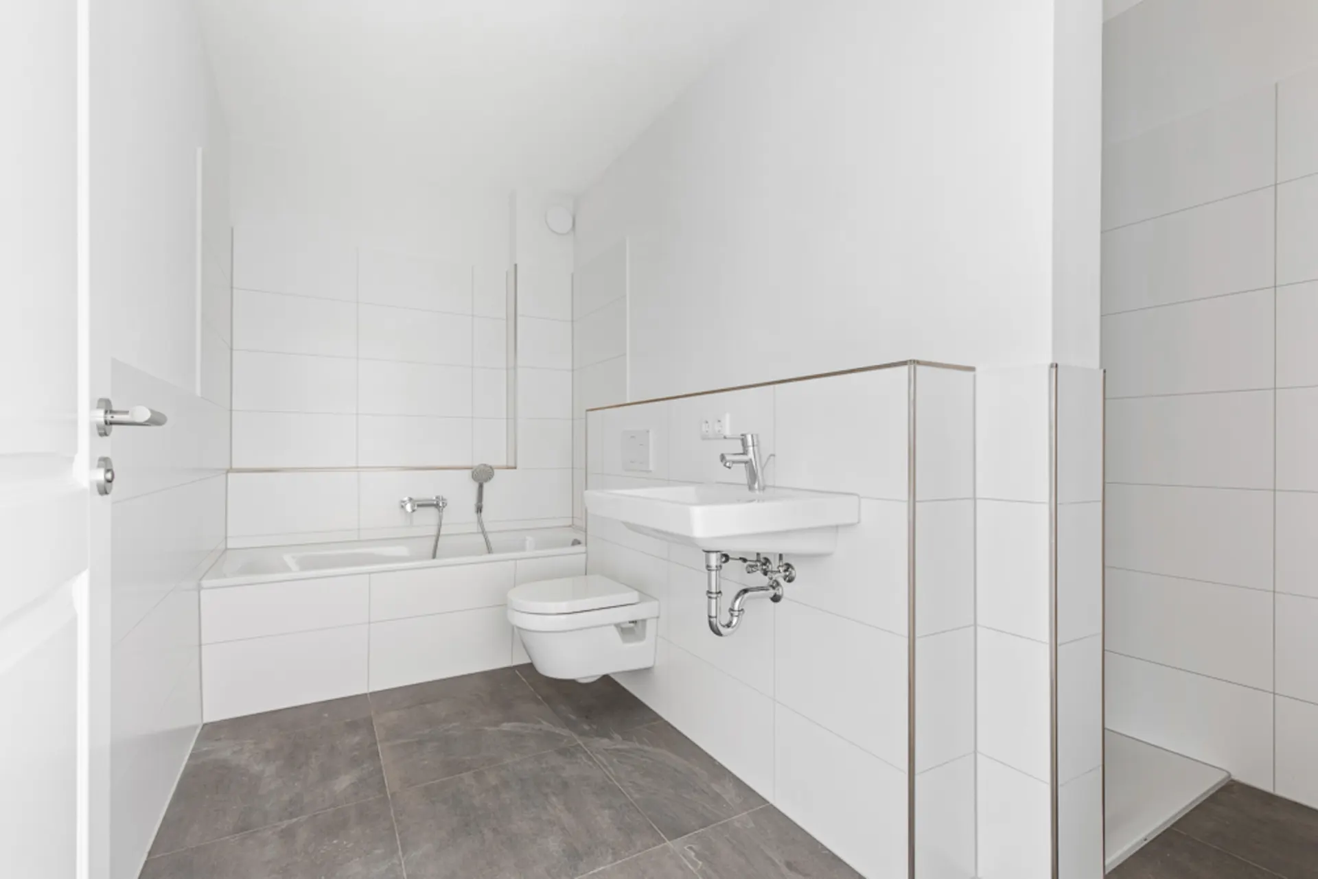 Modernes Bad mit Badewanne, Wand-WC, Waschbecken und bodengleicher Dusche.