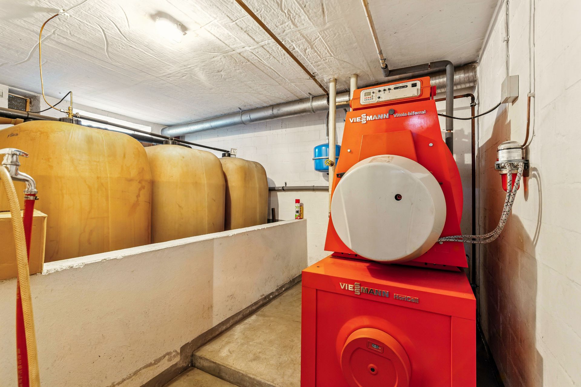 Heizungsraum mit rotem Heizkessel und drei großen Öltanks an der Wand.