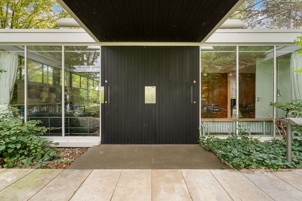 Eingang eines modernen Hauses mit schwarzer Holztür und großen Glasfenstern.