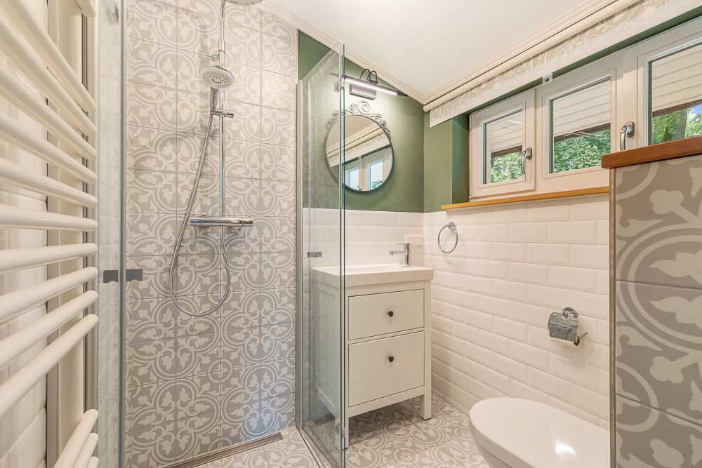 Modernes Badezimmer mit gemusterter Dusche, Waschbecken, Spiegel, Fenster und Toilette.