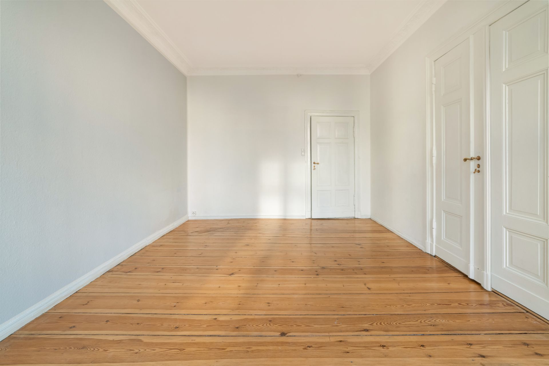 Leerer Raum mit hellen Wänden, Holzboden und drei weißen Türen.