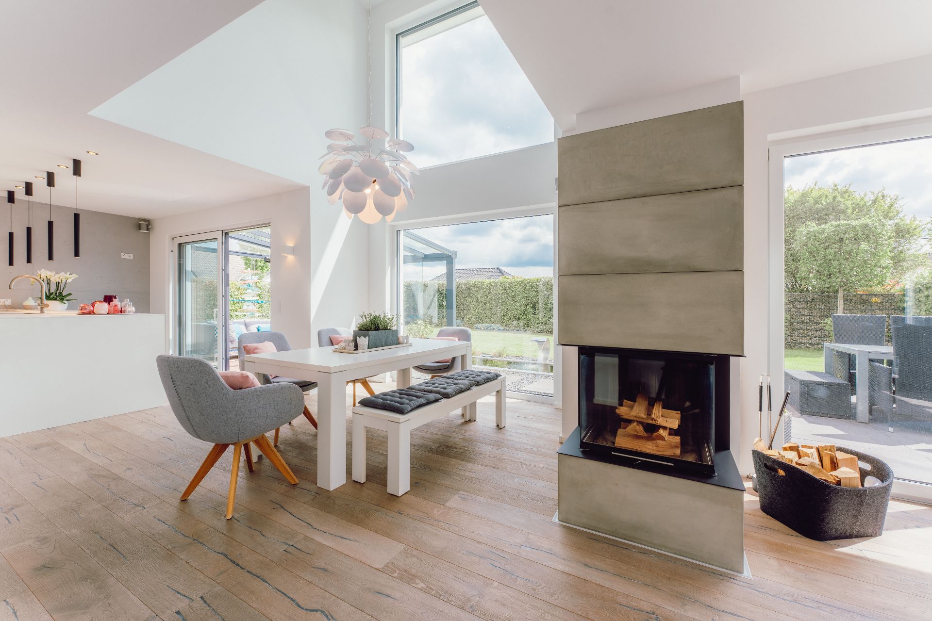 Helles Wohnzimmer mit Esstisch, Kamin, modernen Stühlen und großen Fenstern zum Garten.