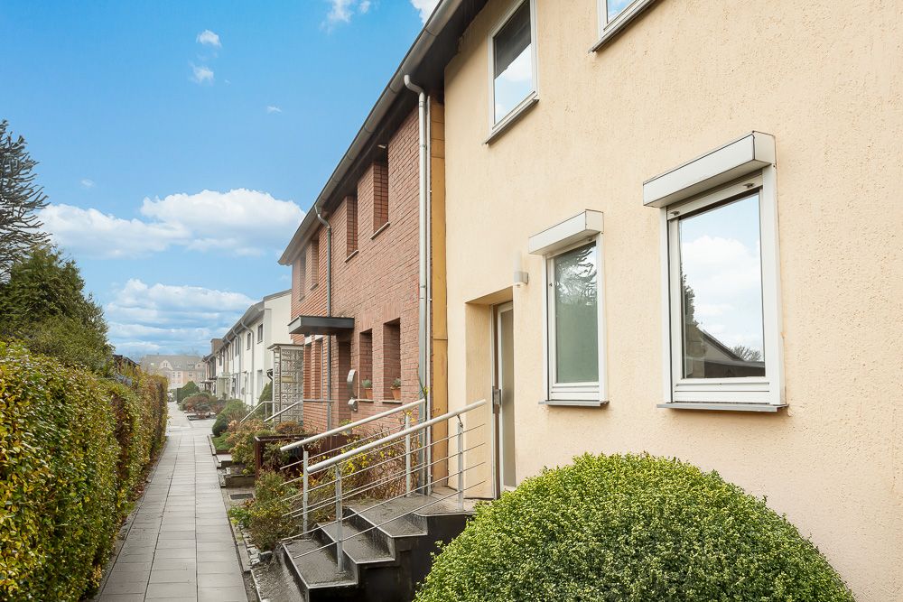 Reihenhäuser mit Vorgärten und Gehweg, aufgenommen bei Tageslicht.