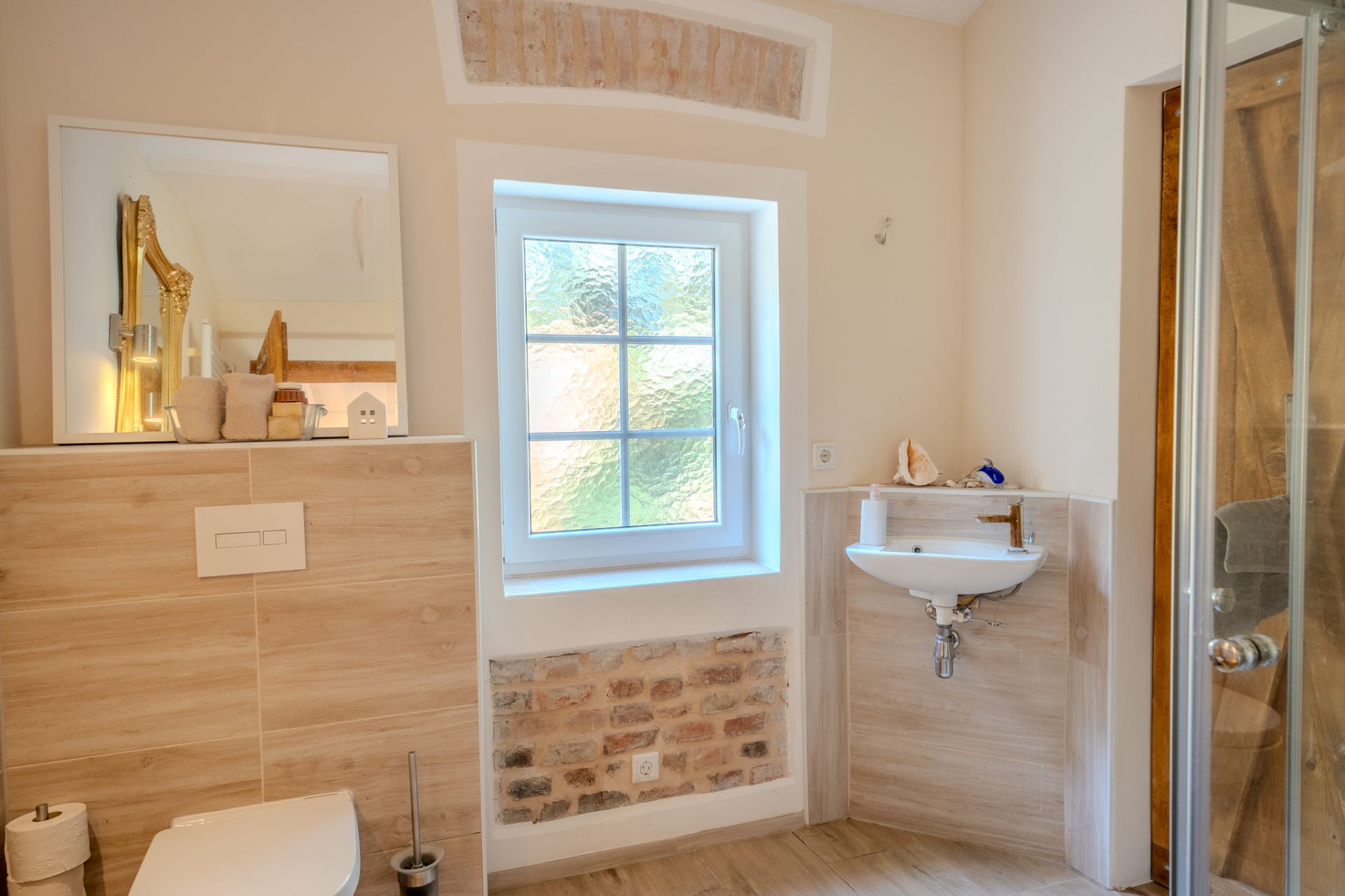 Helles Badezimmer mit Fenster, Toilette, kleinem Waschbecken und Dusche.
