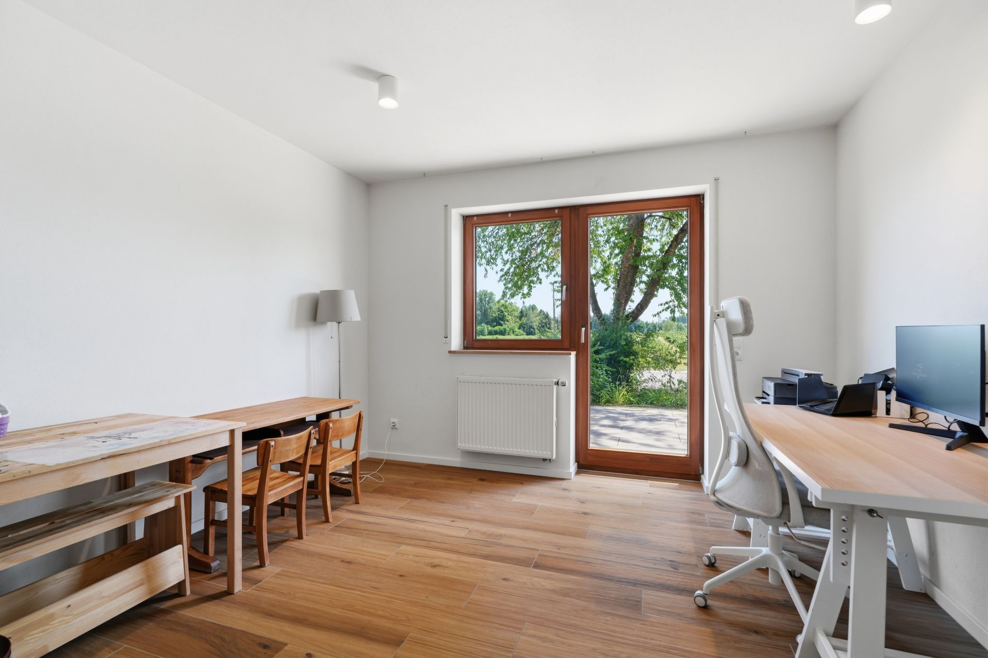 Helles Arbeitszimmer mit Schreibtisch, Holzfußboden und großem Fenster mit Blick auf einen Garten.