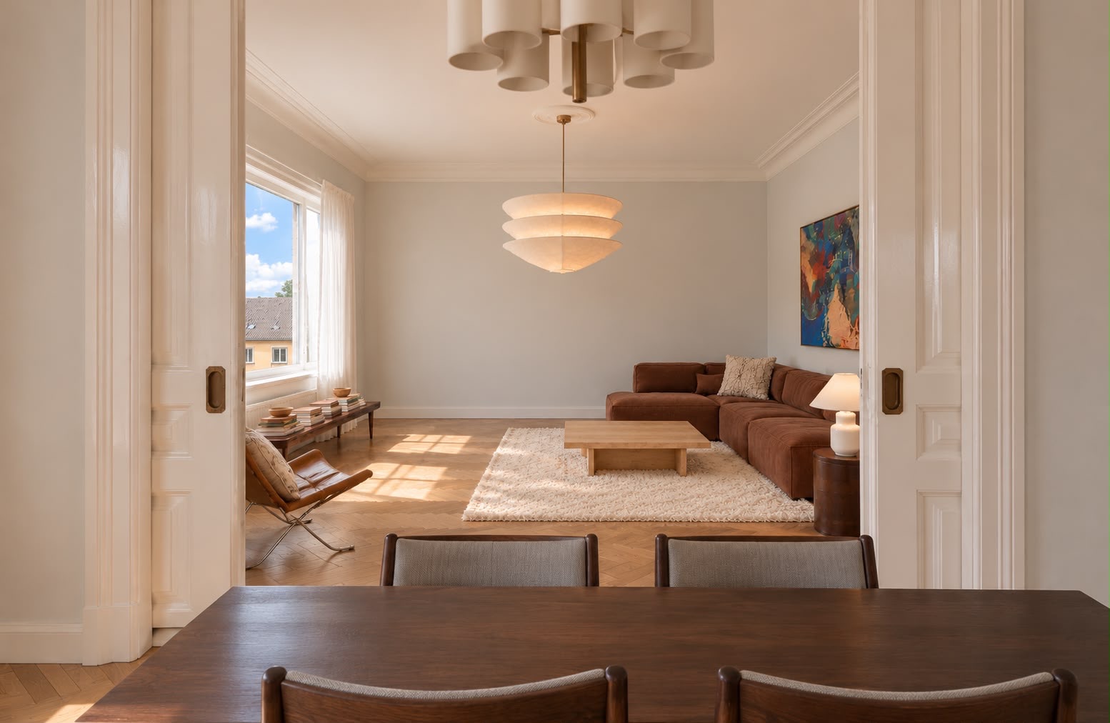 Wohnzimmer mit braunem Sofa, Teppich, Couchtisch und großem Fenster, Essbereich im Vordergrund.