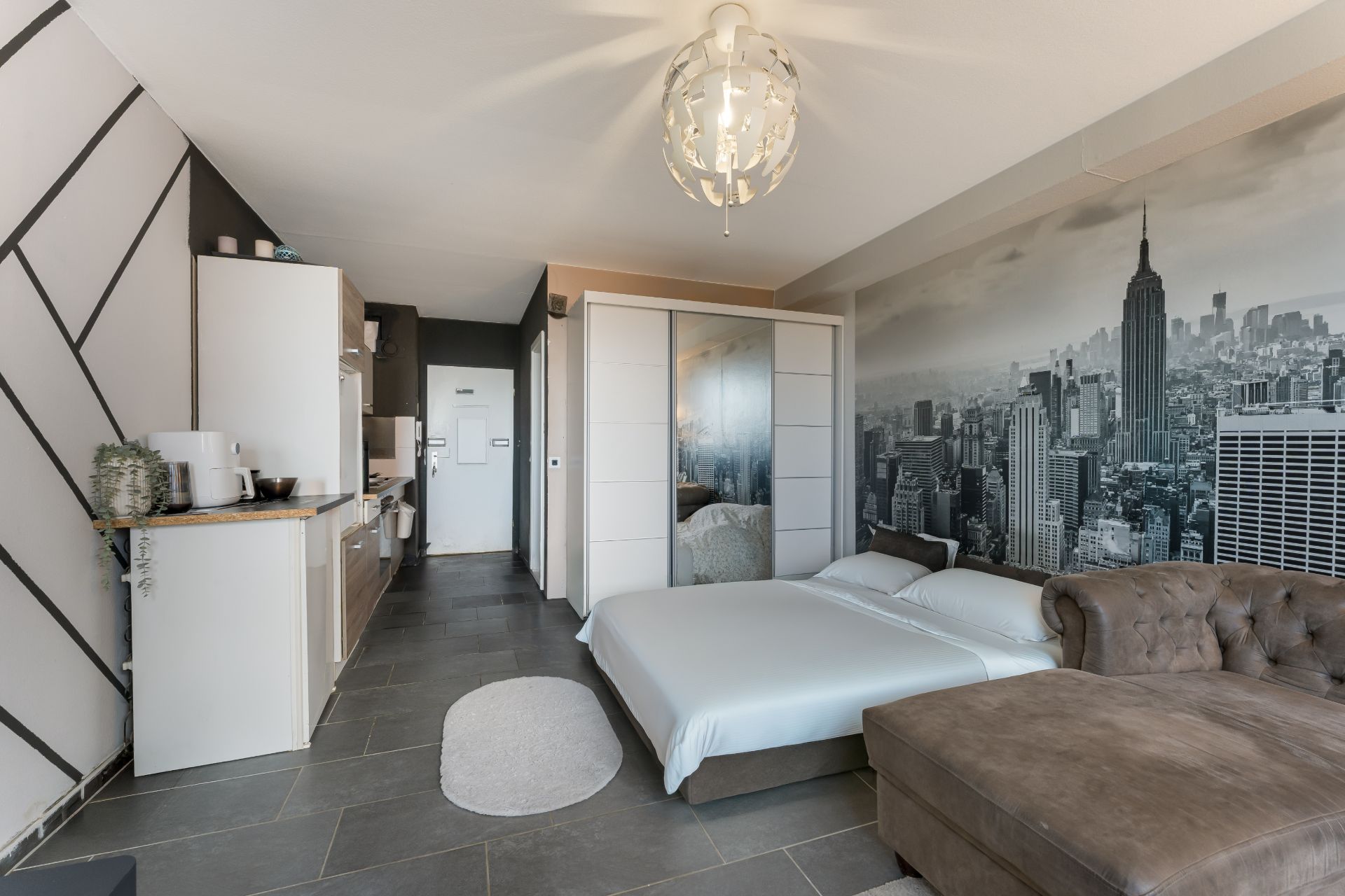 Modernes Studio mit Schlafsofa, Küchenzeile und großem Stadtbild an der Wand.