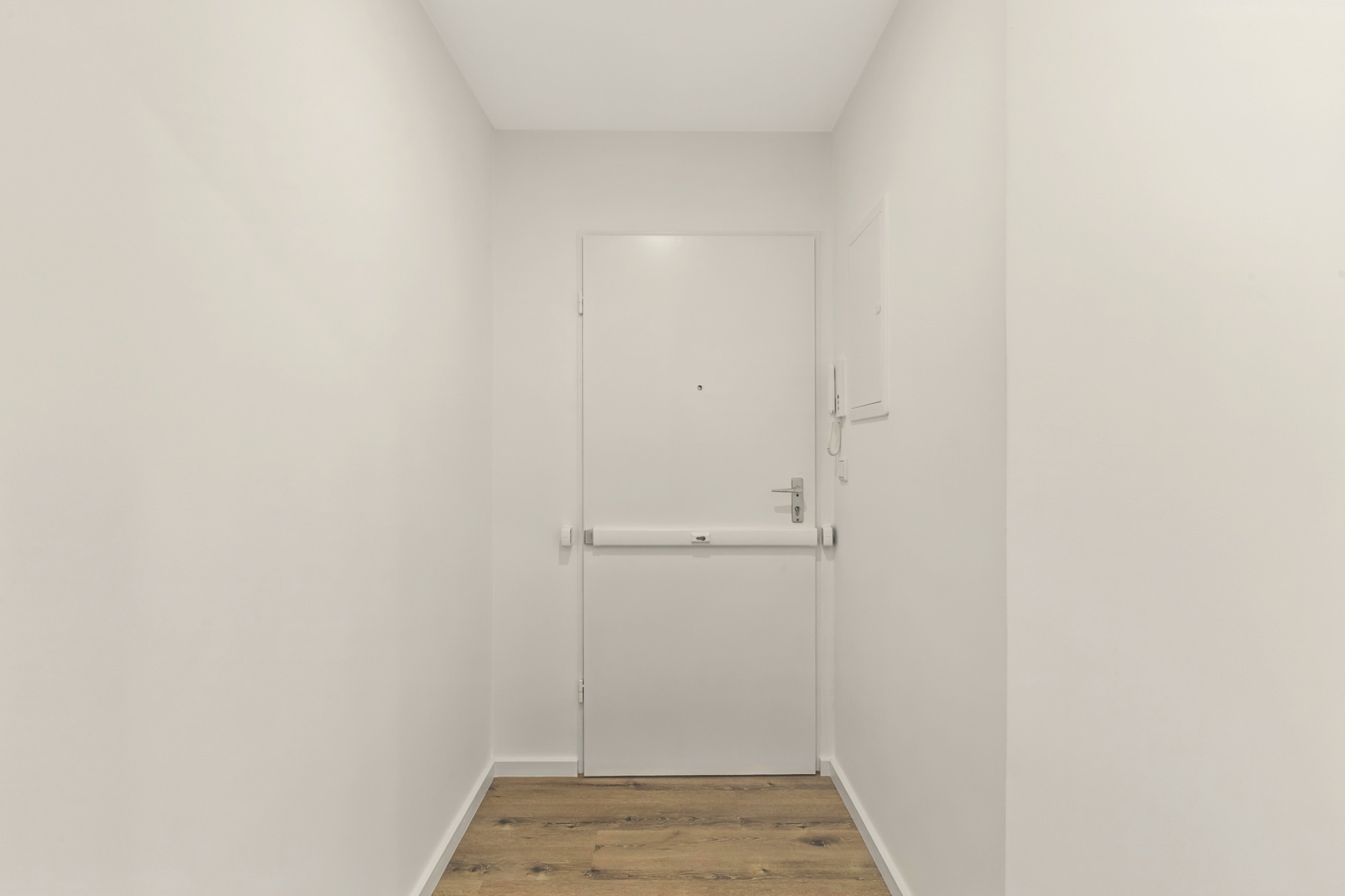 Heller Flur mit weißer Tür und Holzboden.