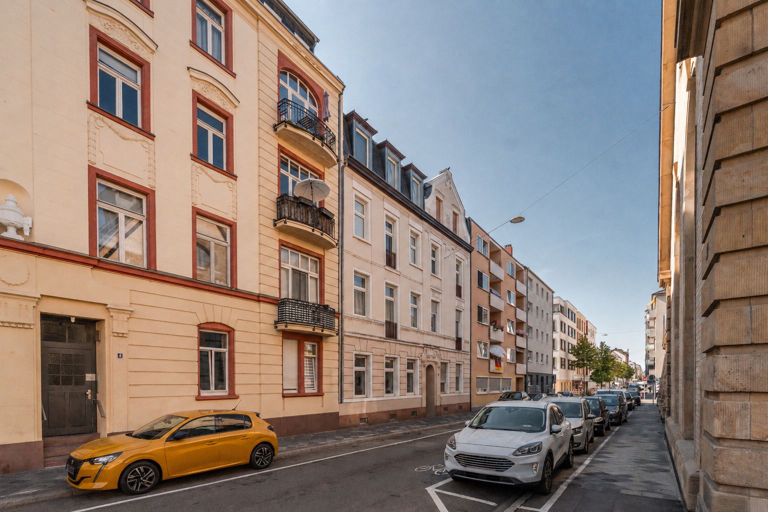 Wohngebäude mit Balkonen an einer ruhigen Straße, geparkte Autos am Straßenrand.