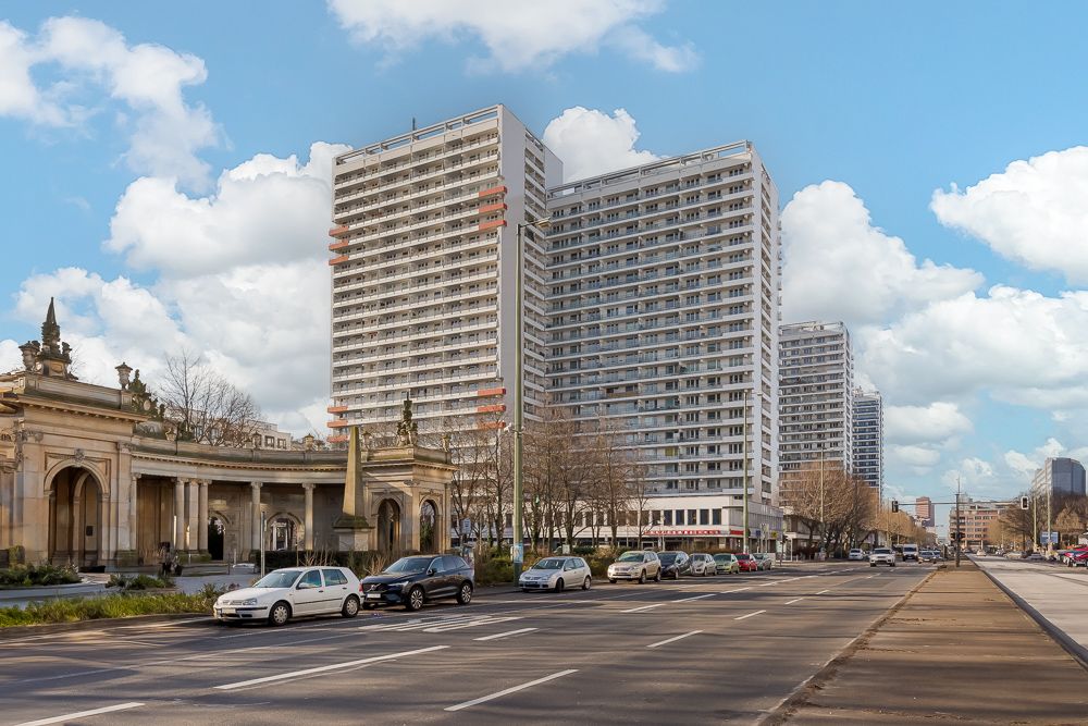 Mehrere hohe Wohngebäude neben einer belebten Straße bei Tageslicht.