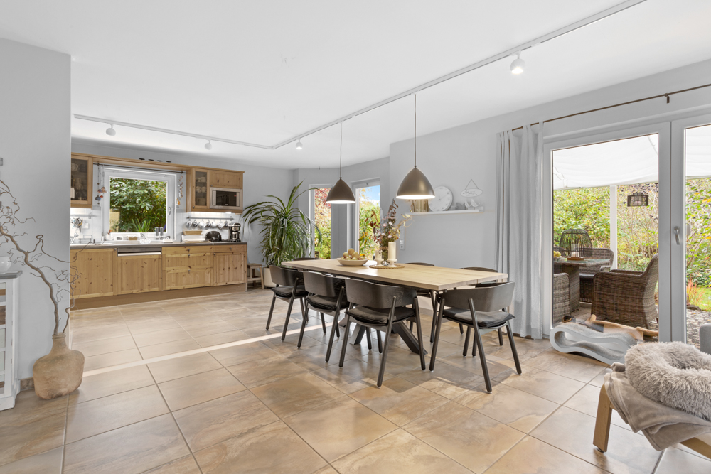 Heller Essbereich mit Holztisch, sechs schwarzen Stühlen, Küche und Zugang zur Terrasse mit Gartenmöbeln.