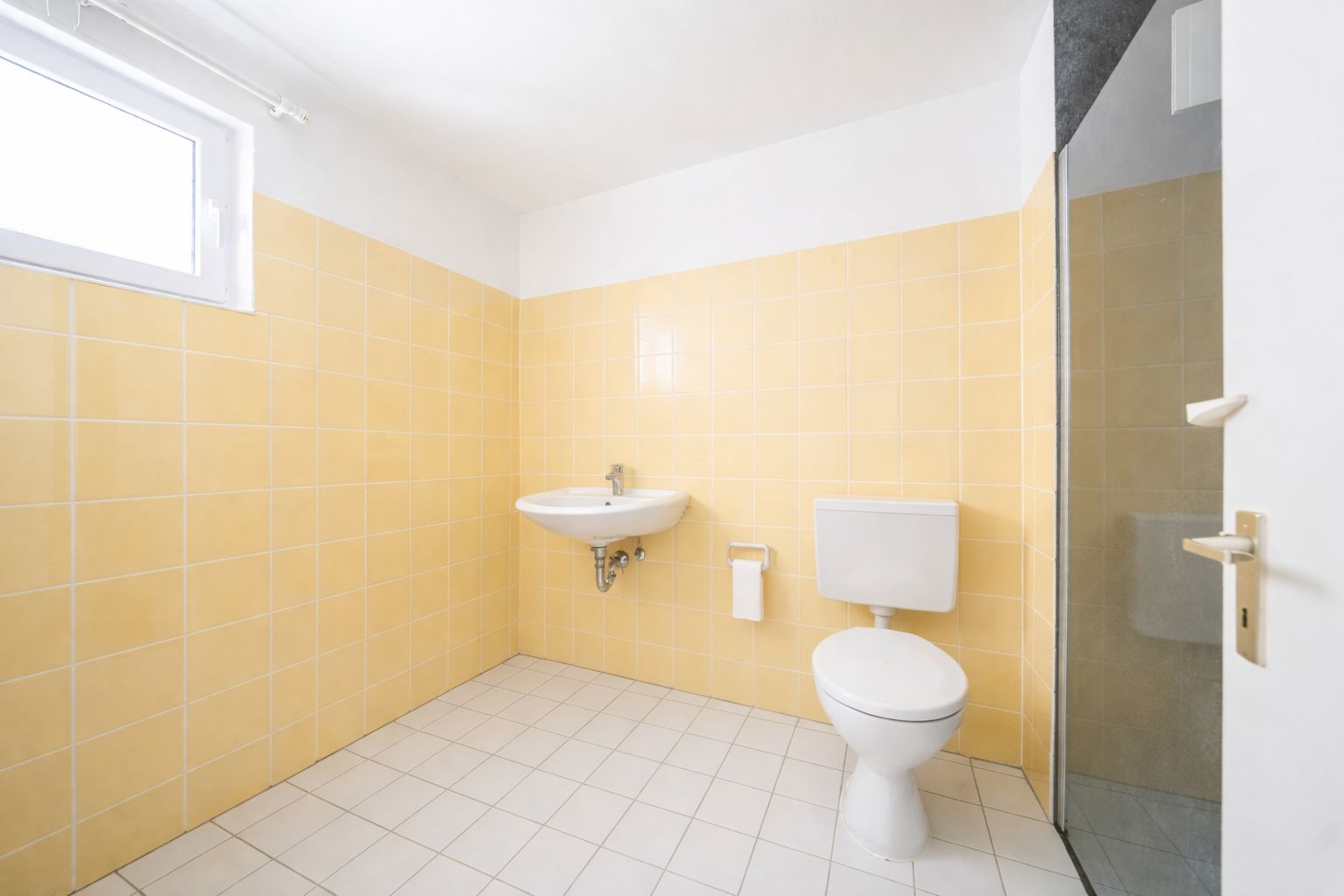Helles Badezimmer mit gelben Fliesen, Fenster, Waschbecken und Toilette.