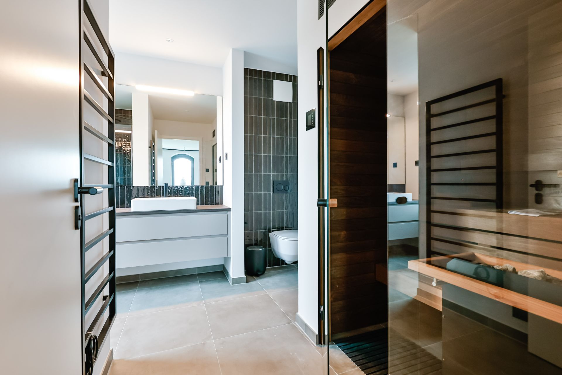 Modernes Badezimmer mit Waschbecken, Toilette und Saunaraum aus Holz.