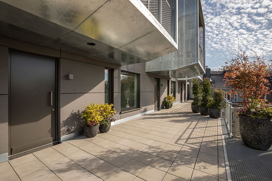 Großer Balkon eines Wohnhauses mit mehreren Blumentöpfen und modernen Fassaden.