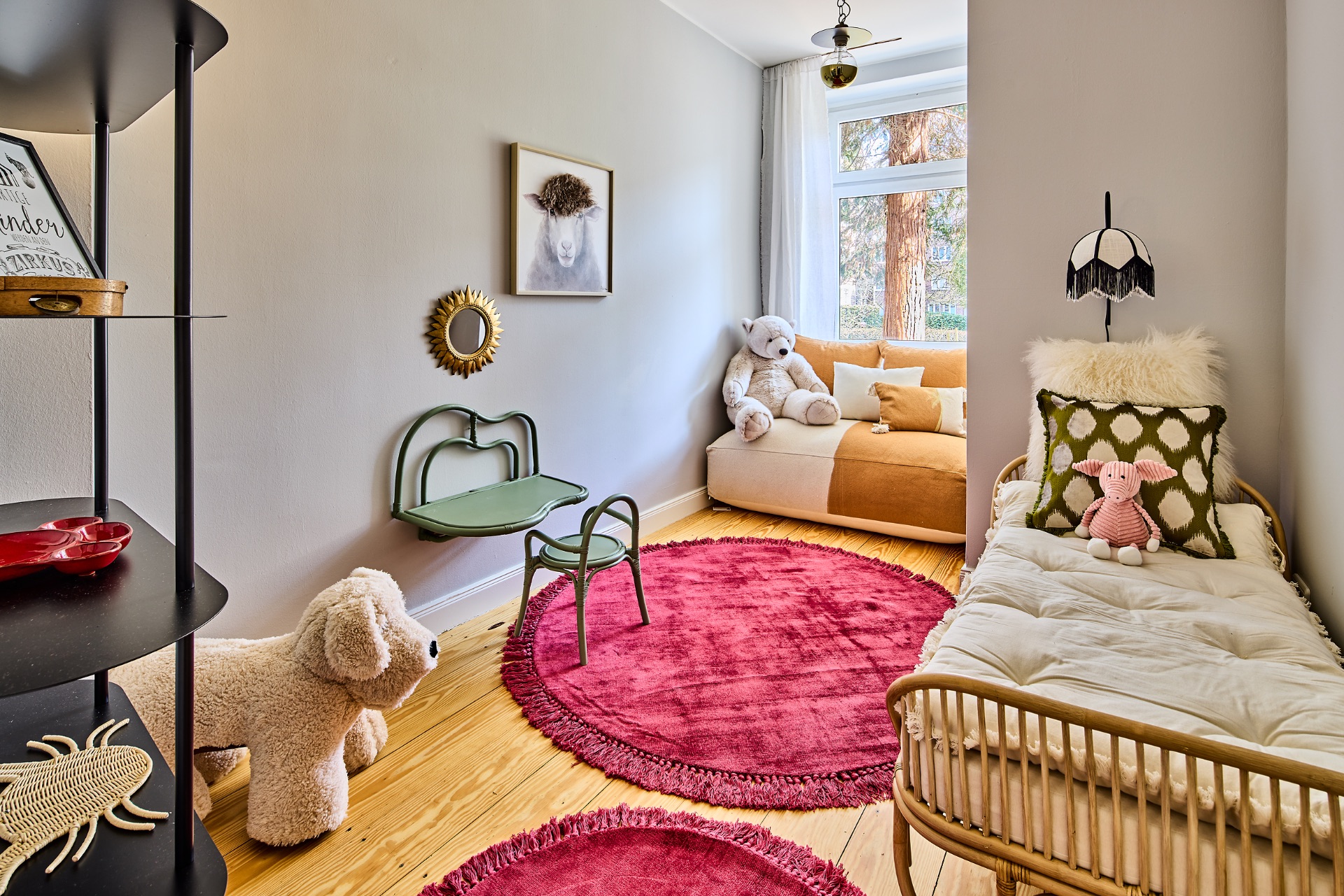 Kinderzimmer mit Spielzeugtieren, zwei runden roten Teppichen, Bett und Sofa bei großem Fenster.