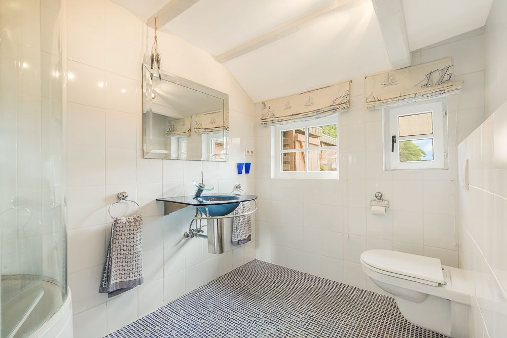 Modernes Badezimmer mit runder Dusche, Wandwaschbecken, großem Spiegel und zwei Fenstern.