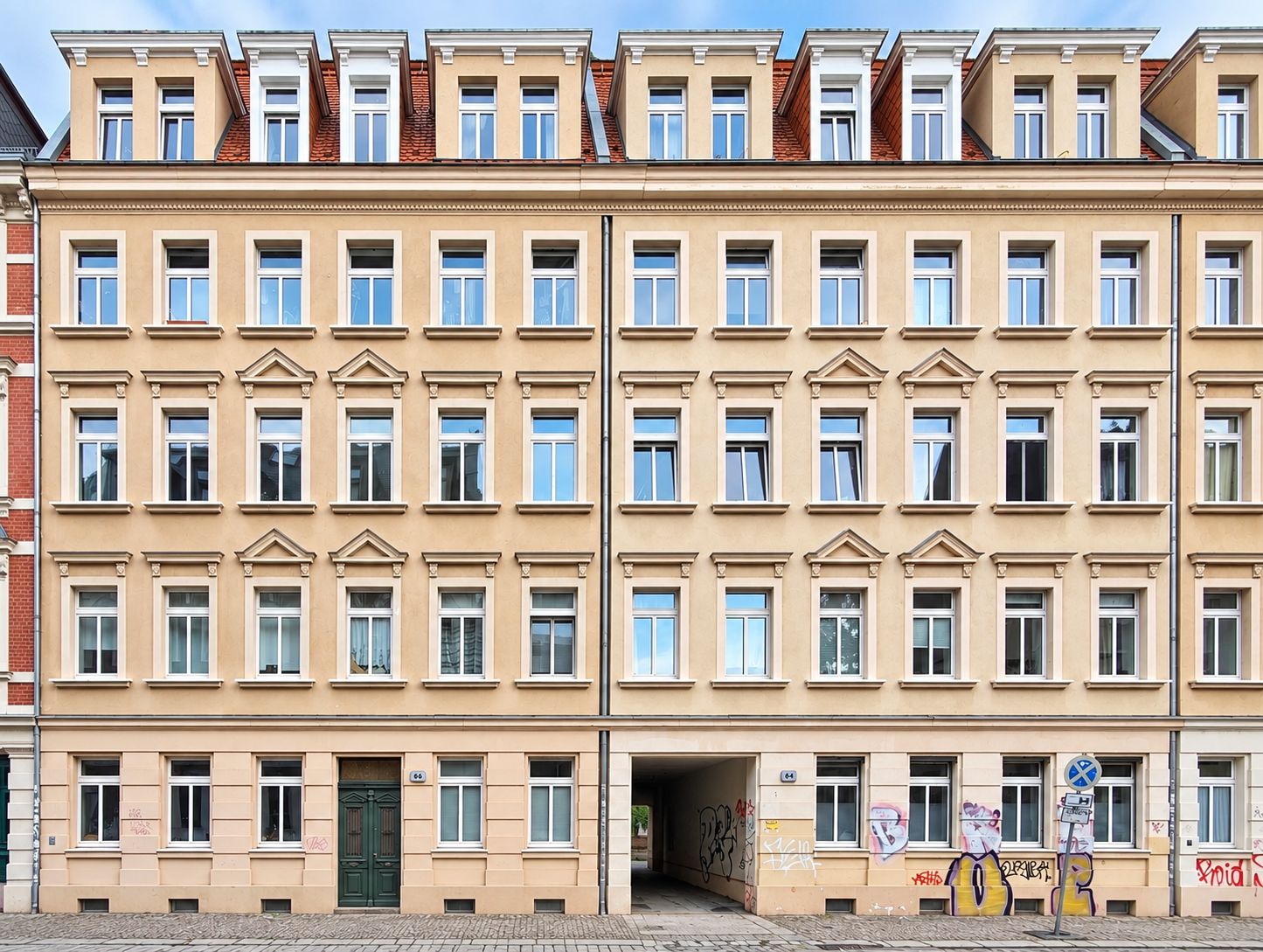 Fassade eines mehrstöckigen Wohnhauses mit vielen Fenstern und einem Torbogen in der Mitte.