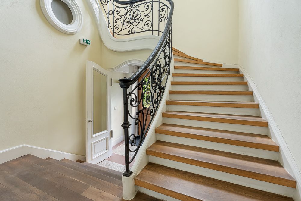 Holztreppe mit verziertem Geländer in einem hellen Wohnhausflur.
