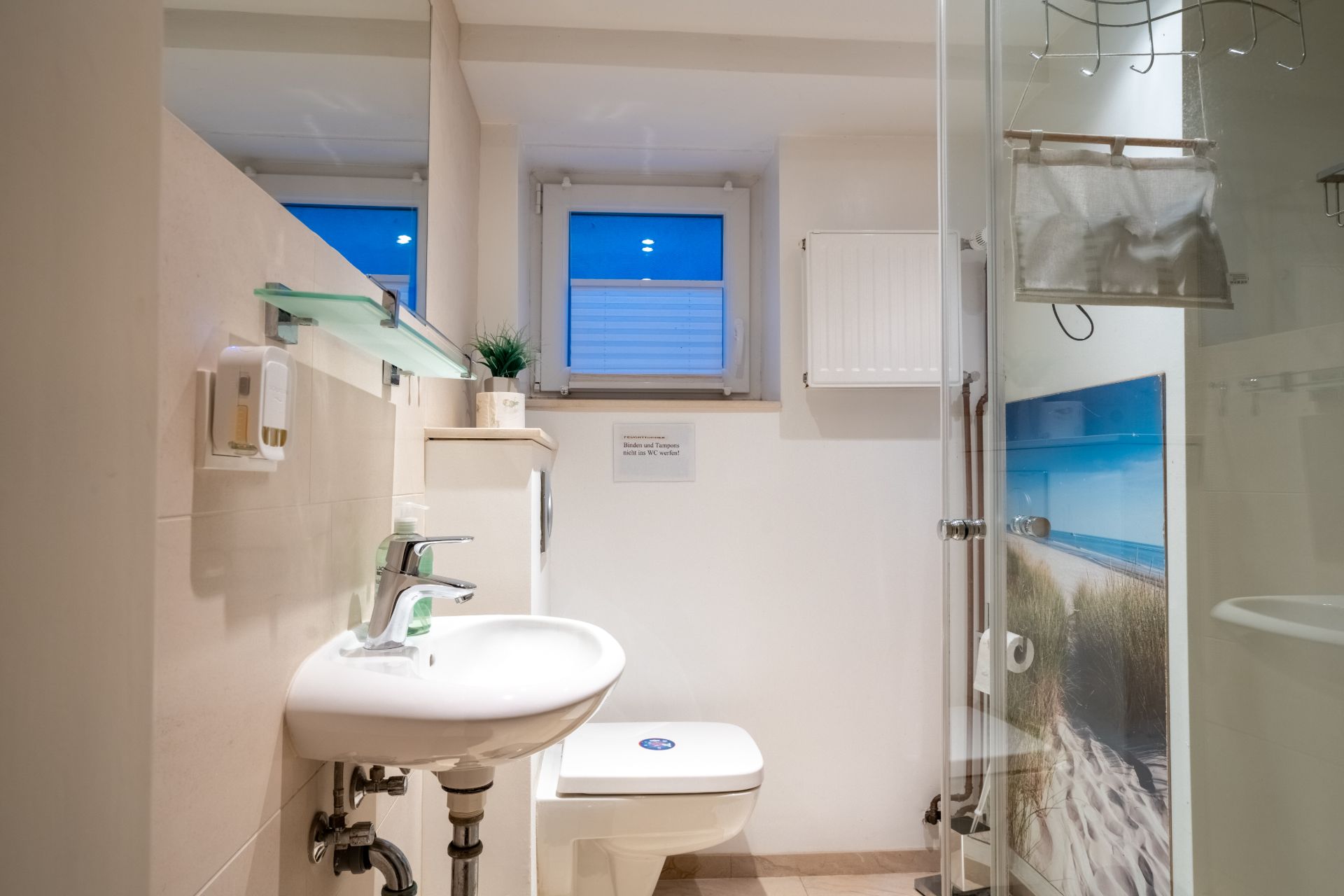 Helles Badezimmer mit Waschbecken, Toilette, Dusche und Fenster.