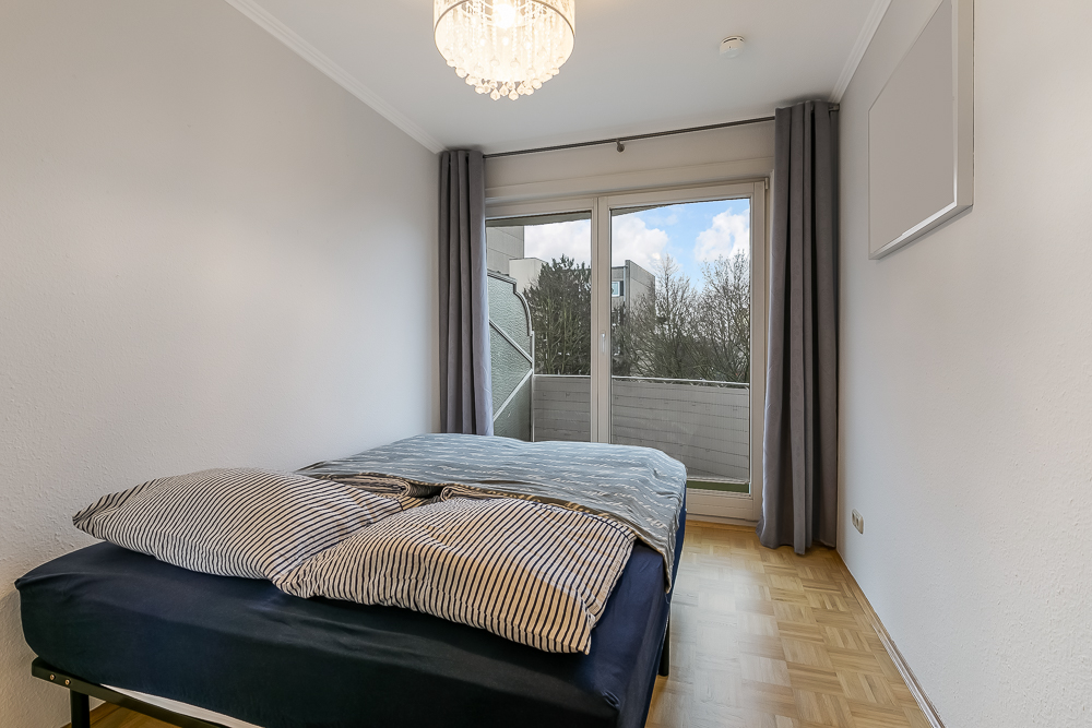 Schlafzimmer mit Doppelbett, Holzboden und Fenster mit Blick auf einen Balkon.