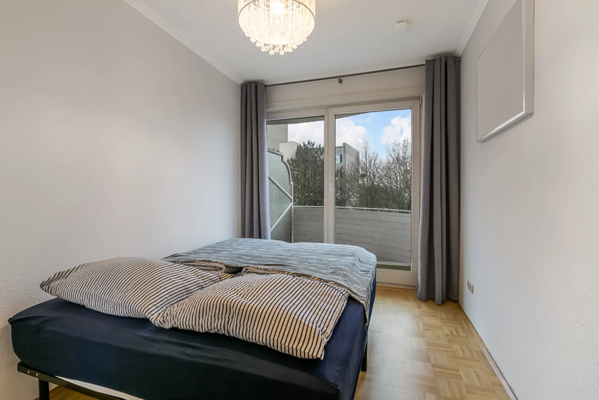 Schlafzimmer mit Doppelbett, Holzboden und Fenster mit Blick auf einen Balkon.