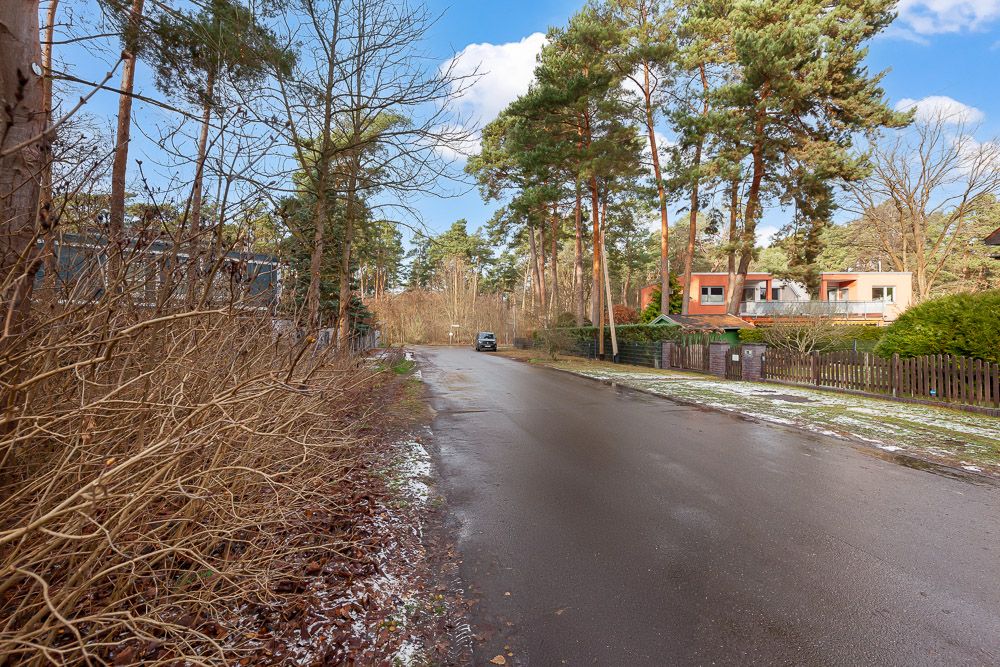 Ruhige Wohnstraße mit Häusern, Bäumen und einem geparkten Auto, etwas Schnee am Straßenrand.
