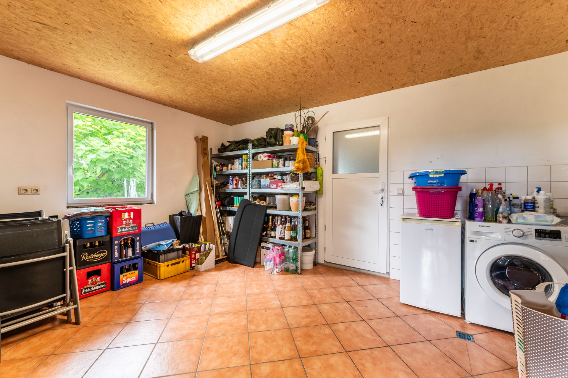 Hauswirtschaftsraum mit Regalen, Waschmaschine, Getränkekisten und Putzmitteln.