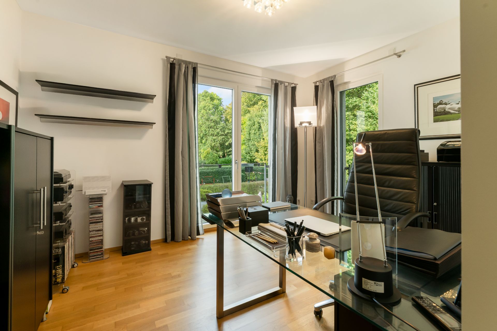 Modernes Arbeitszimmer mit Schreibtisch, Stuhl, Regalen und großen Fenstern mit Blick ins Grüne.