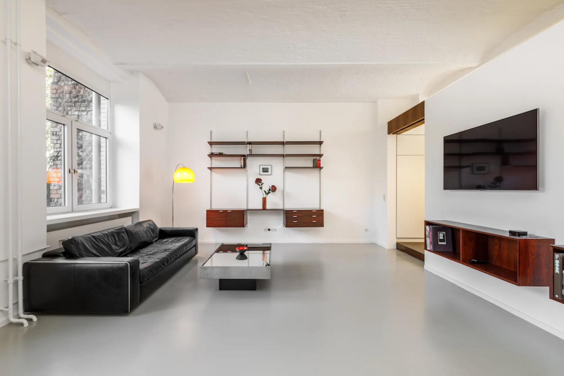 Modernes Wohnzimmer mit schwarzem Sofa, Wandregal, Glastisch und Flachbildfernseher.