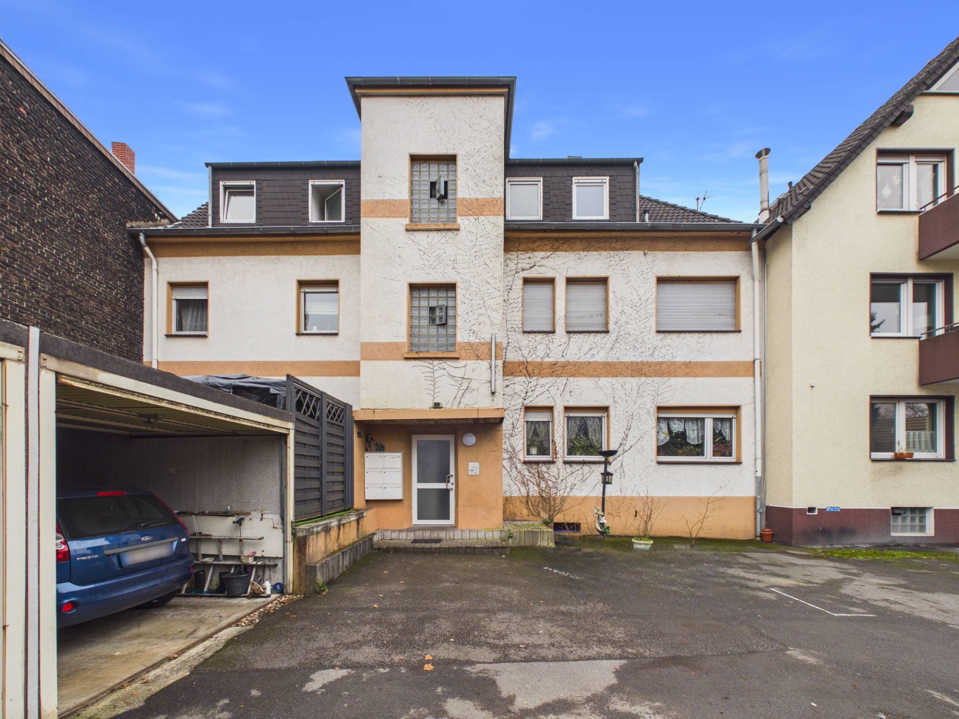 Vorderansicht eines dreistöckigen Wohnhauses mit Hof und angrenzender Garage.