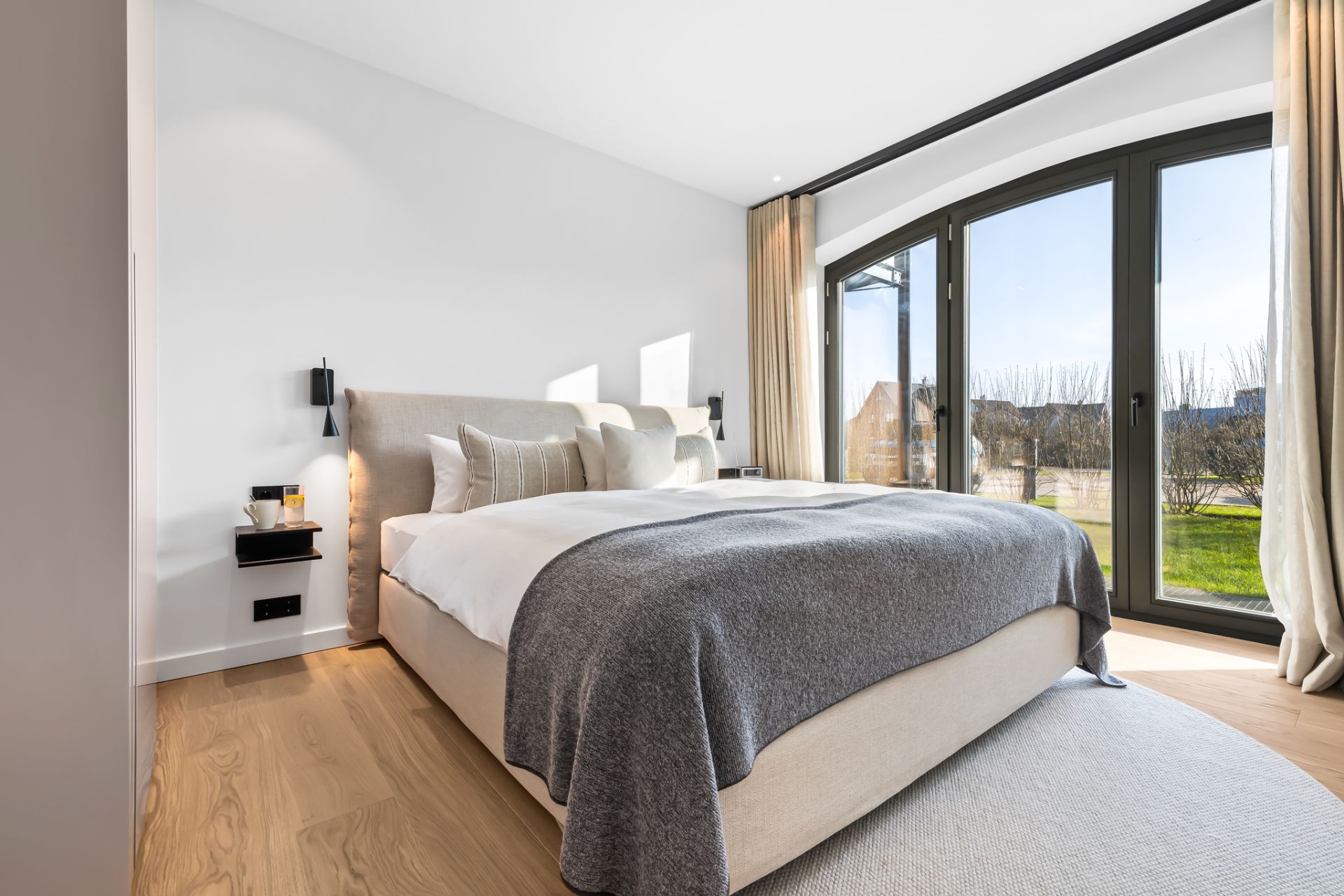 Modernes Schlafzimmer mit Doppelbett, großen Fenstern und Blick auf einen Garten.