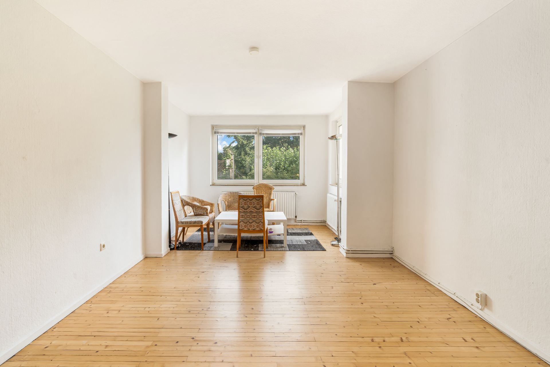 Helles Wohnzimmer mit Holzboden, Tisch und vier Stühlen vor einem großen Fenster.