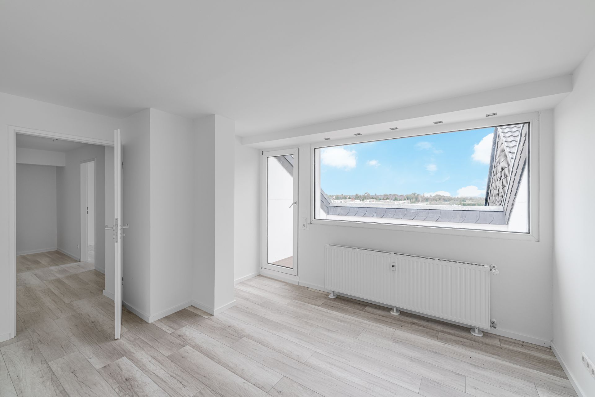 Heller Raum mit großem Fenster, Heizkörper und Holzfußboden, Blick ins Freie.