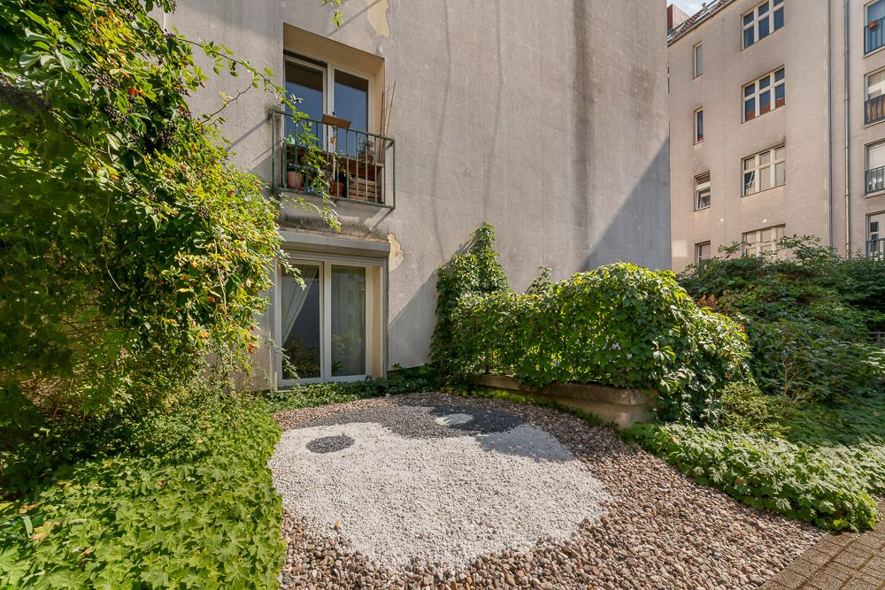 Grüner Innenhof mit Bewuchs, Kiesfläche und Zugang zu einem Balkon und einer Terrassentür.