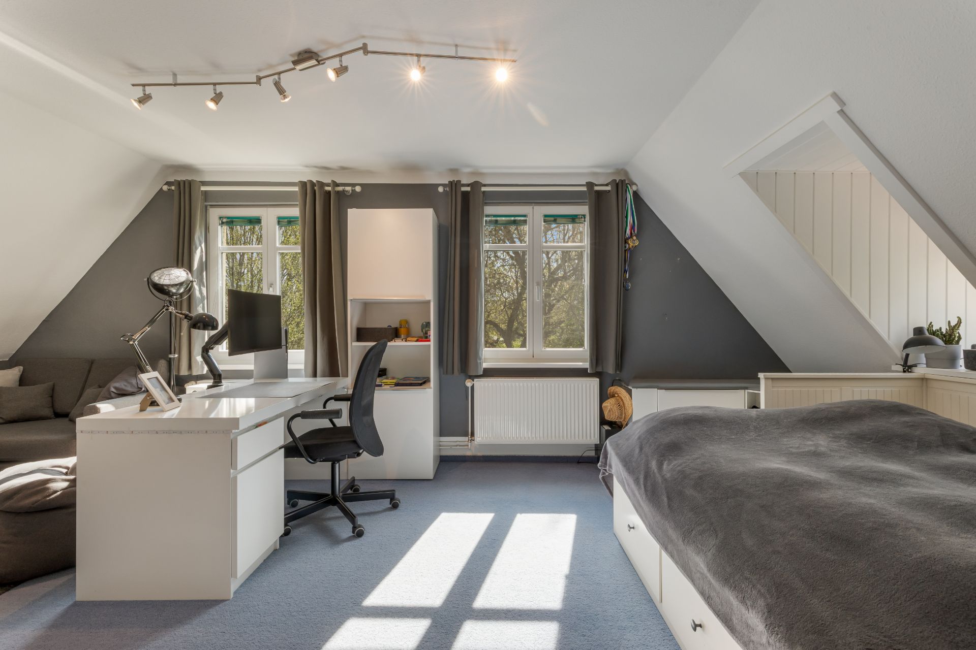 Helles Schlafzimmer mit Schreibtisch, Bett und großen Fenstern, modern eingerichtet.