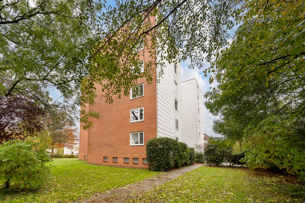 Mehrstöckiges Wohngebäude mit Ziegel- und weißer Fassade, umgeben von Bäumen und Rasen.
