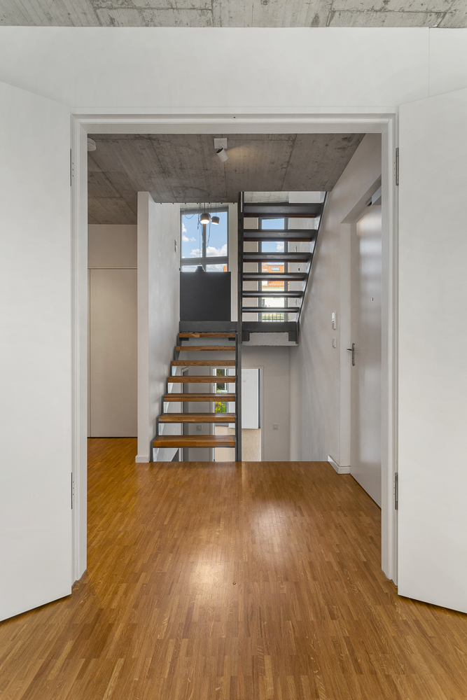 Moderner Flur mit Holzfußboden und offener Treppe, die zu einem Fenster mit Ausblick führt.