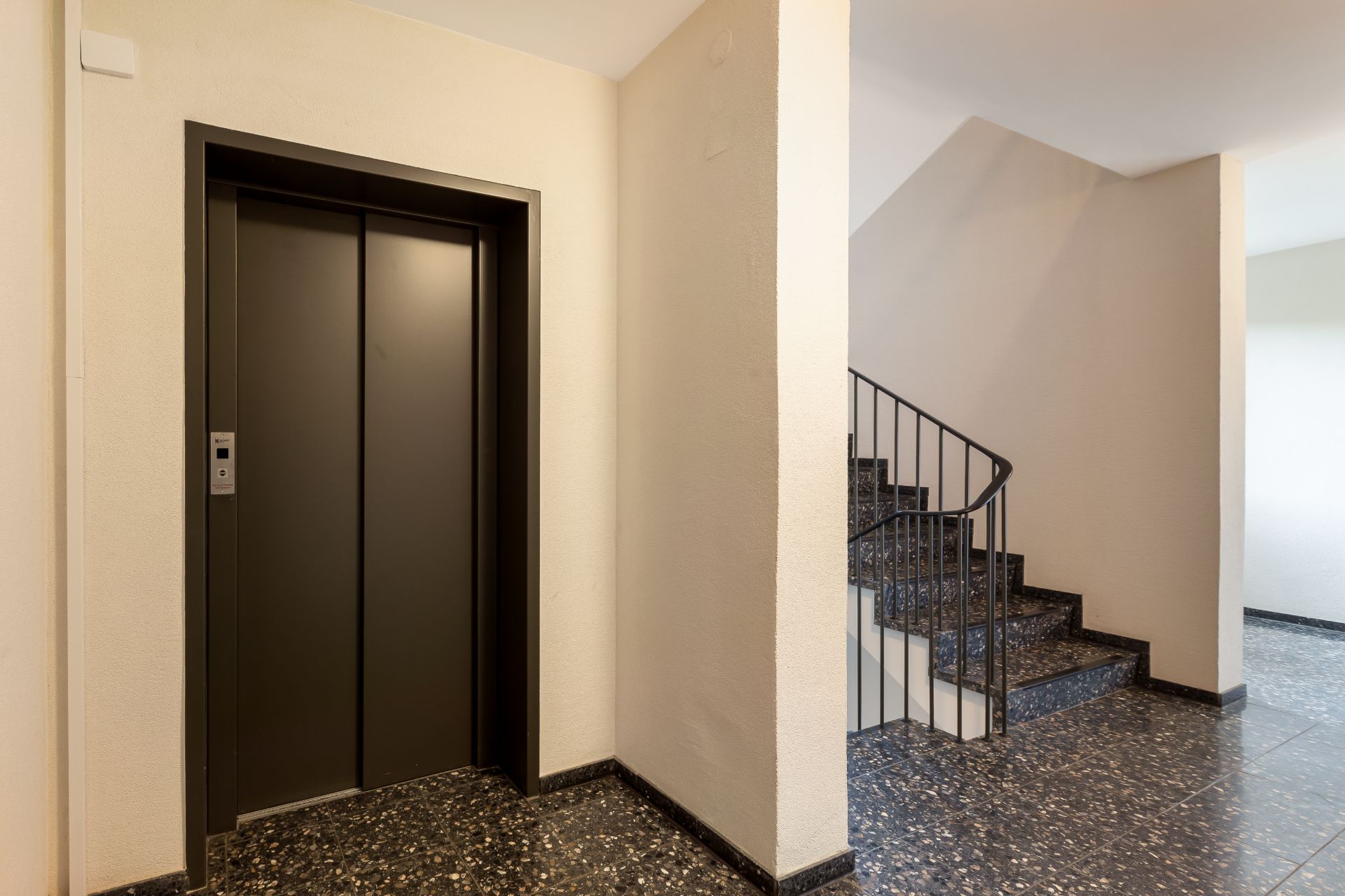 Lift mit geschlossener Tür neben einer Treppe in einem Wohnhausflur.