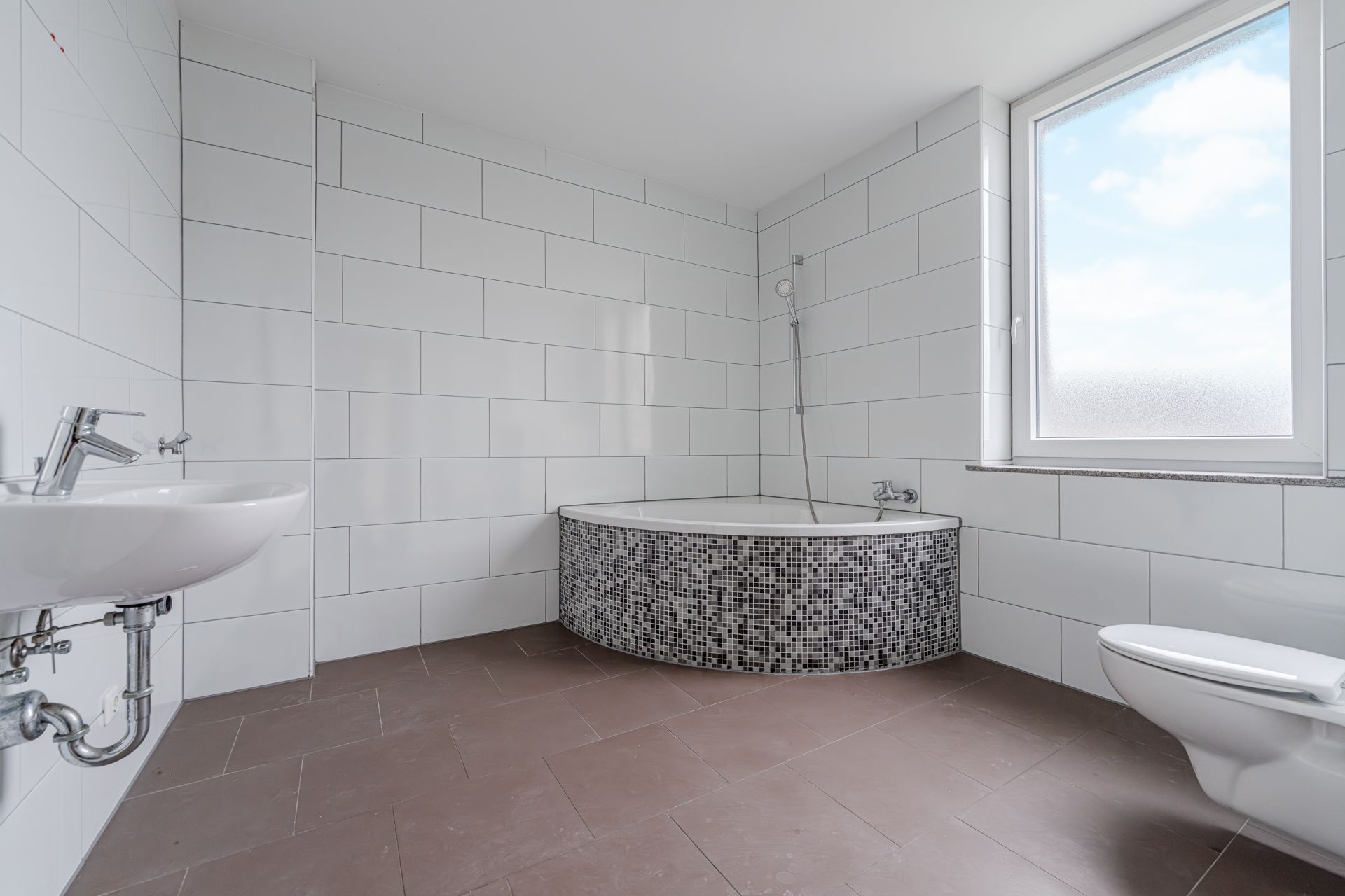 Helles Bad mit Eckbadewanne, Waschbecken, Toilette und großem Fenster.