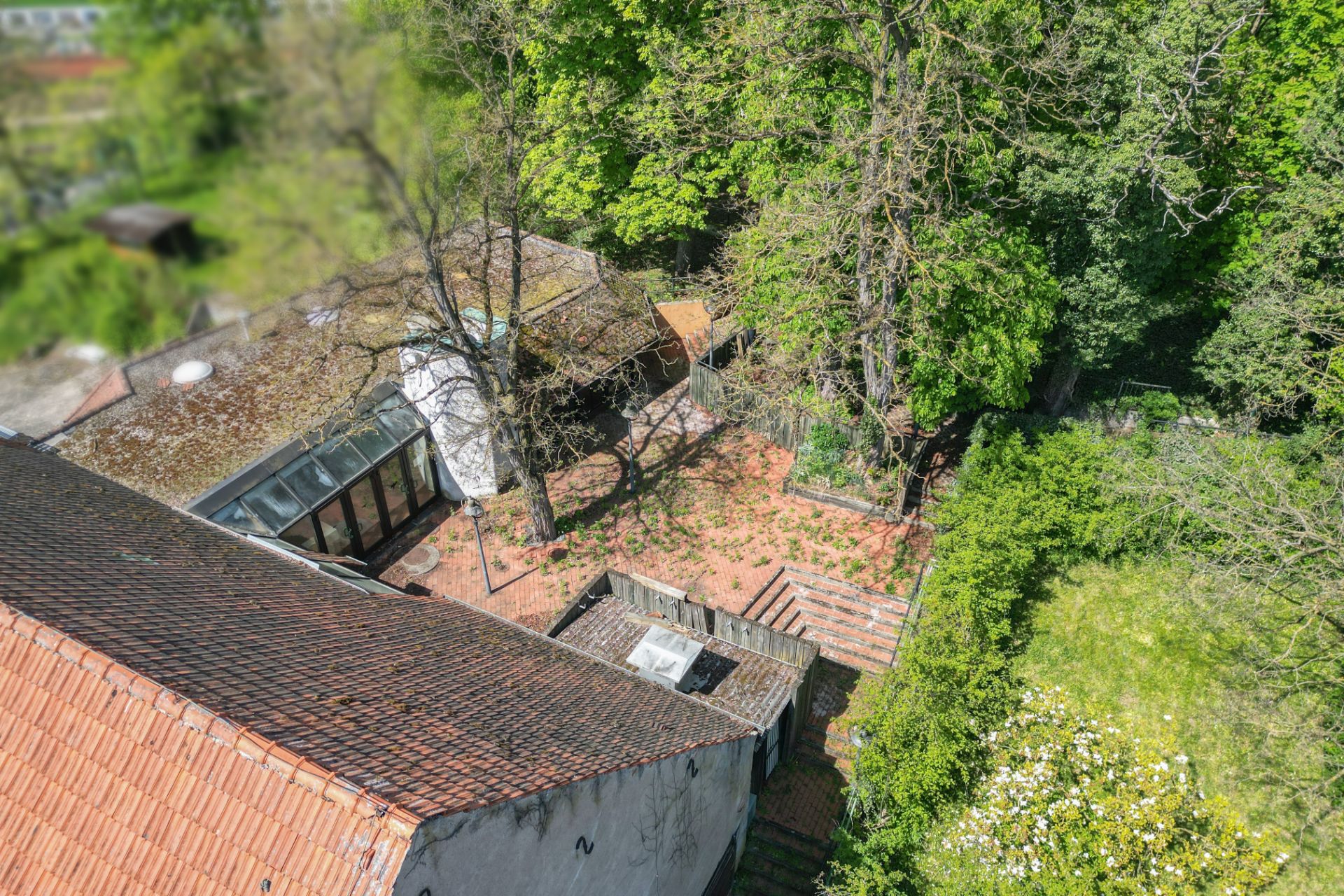 Luftaufnahme eines Hauses mit Ziegeldach und angrenzender Terrasse im Grünen.