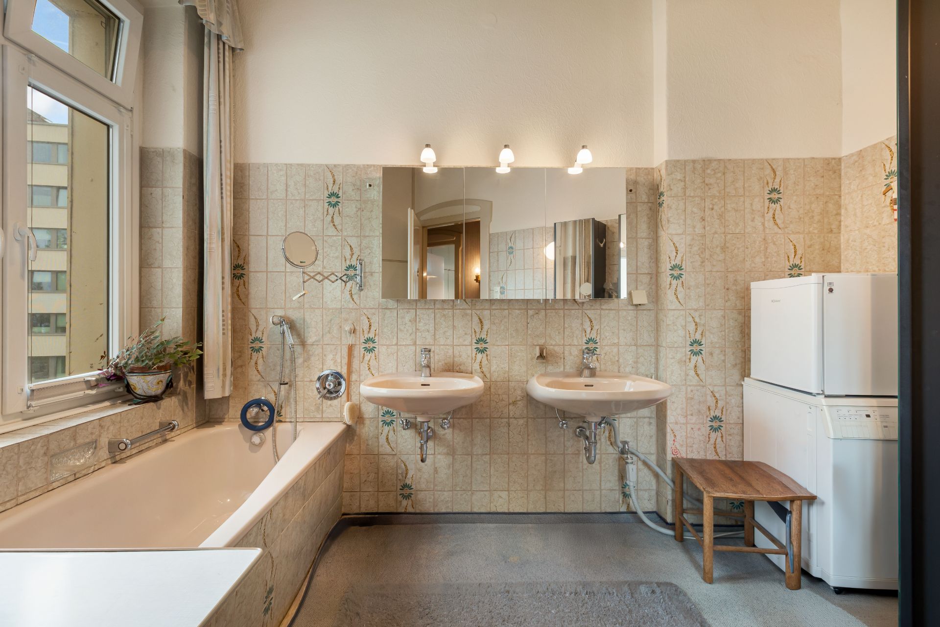 Helles Badezimmer mit Badewanne, zwei Waschbecken, Spiegeln, Fenster und Waschmaschine mit Trockner.