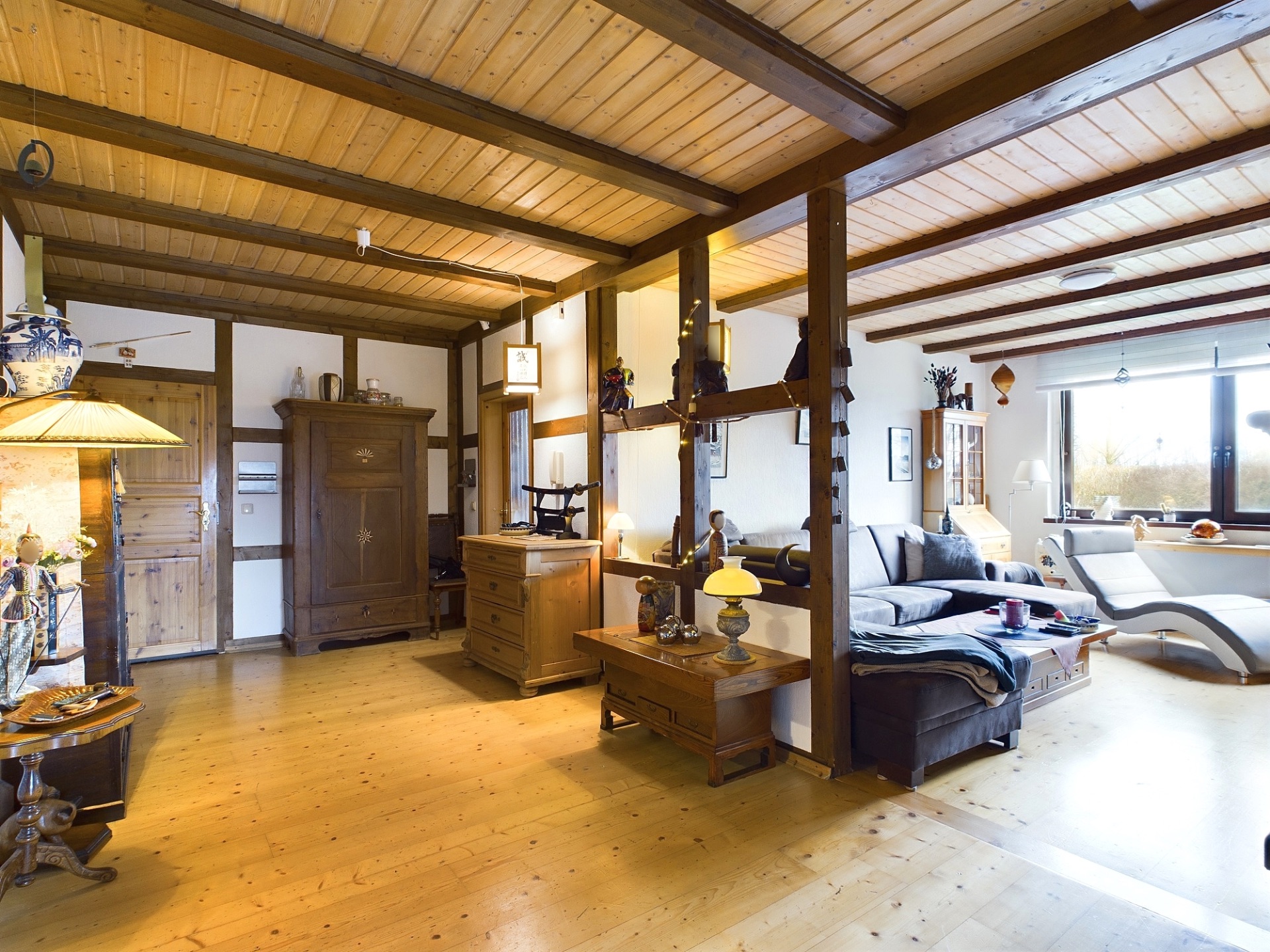 Helles Wohnzimmer mit Holzbalkendecke, Holzmöbeln und großem Fenster.